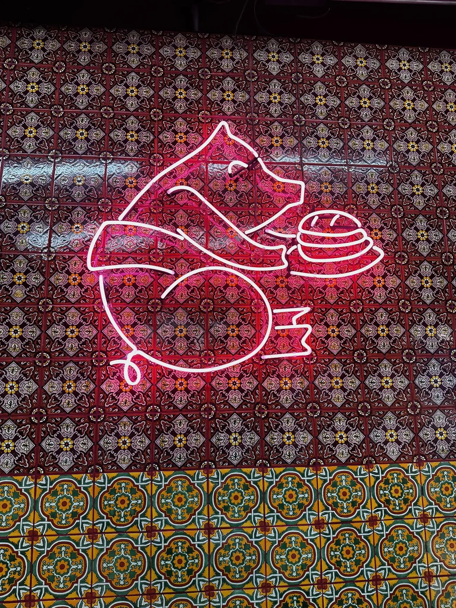A pink neon sign of a pig carrying a torta on a patterned wall.