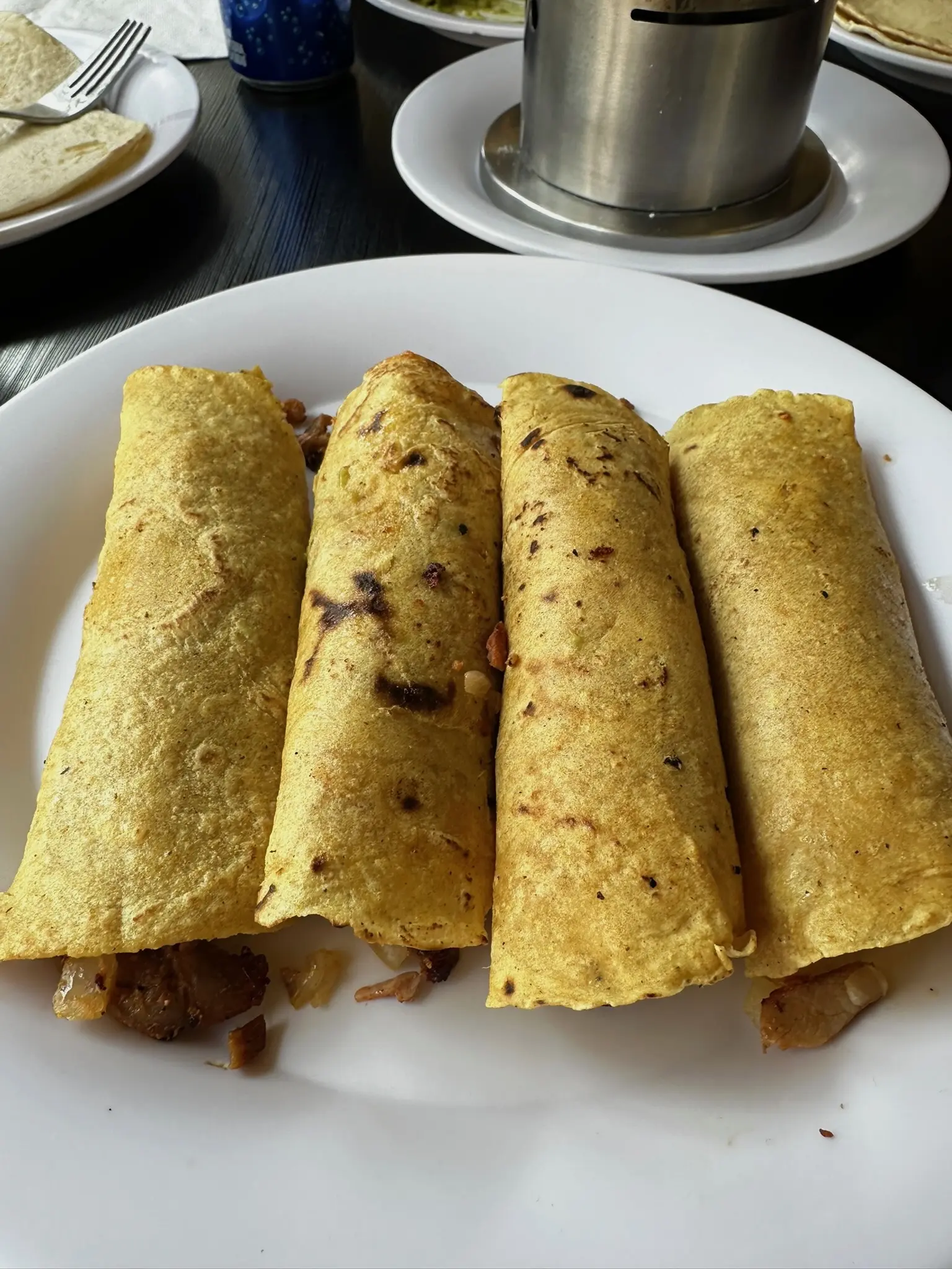 Four al pastor tacos rolled up next to each other on a white plate.
