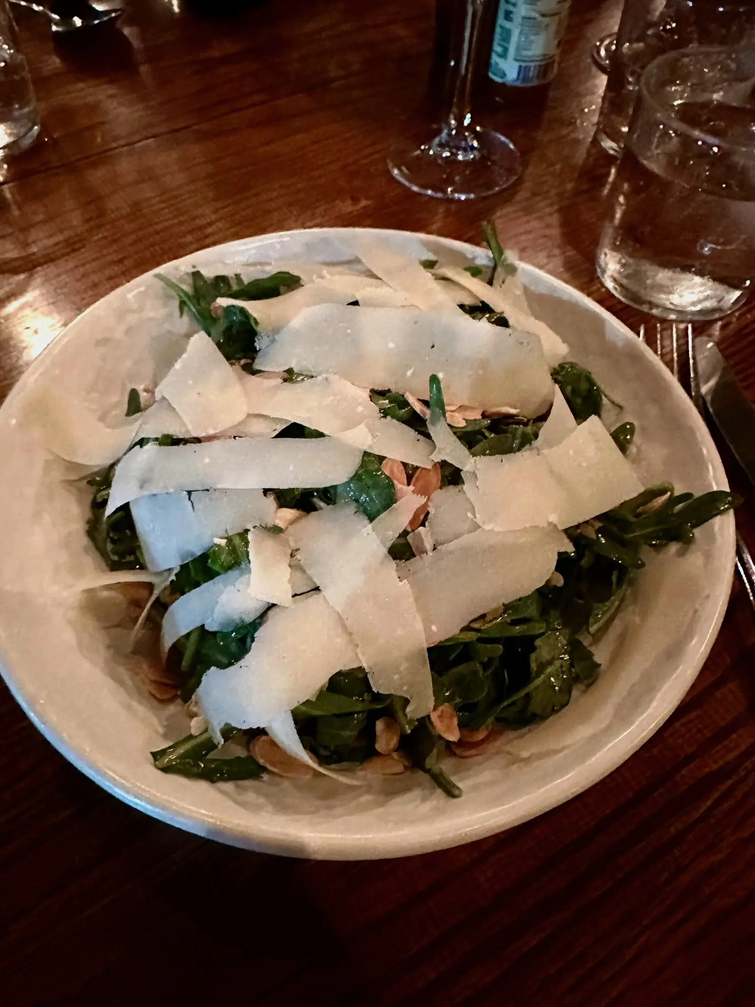 A circular white plate with arugula and large, wide shavings of Parmesan cheese