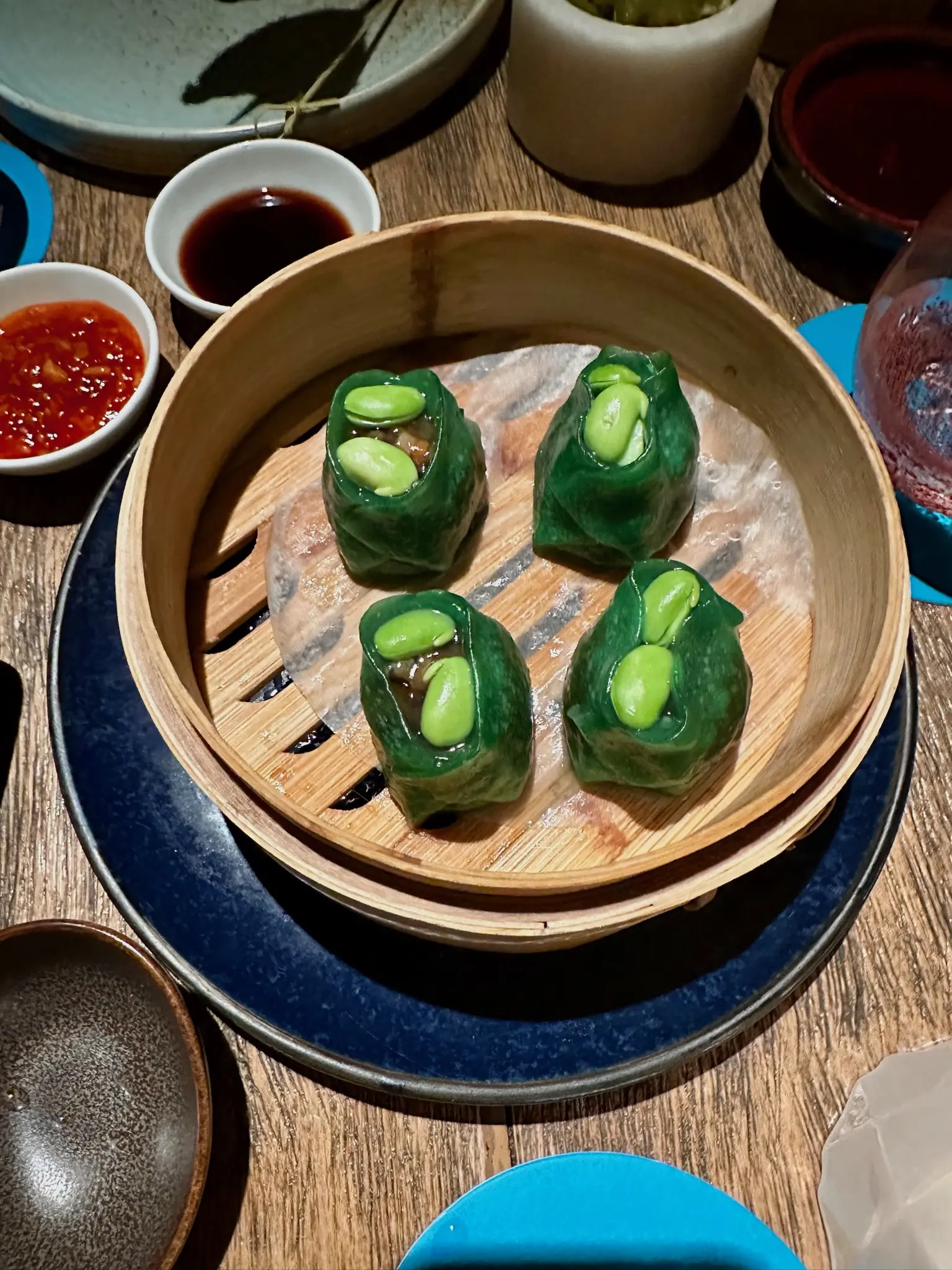 In a bamboo steamer basket sit four green dumplings with two green edamame means sitting in the top.