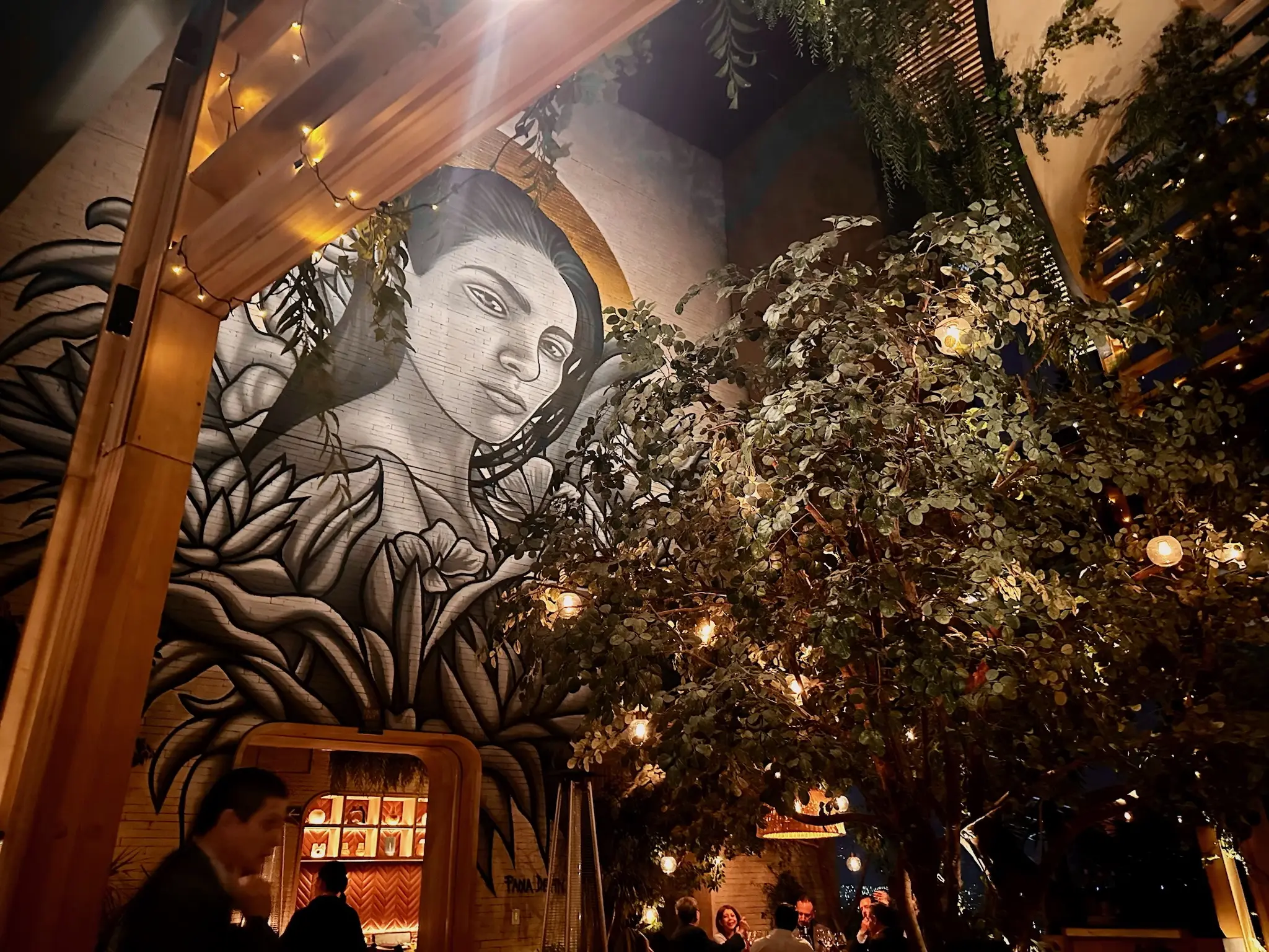 A mural of a woman with long black hair is on a wall with a large lush tree in the center of the room.